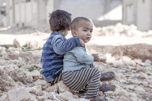 On 25 December 2015 in Aleppo in the Syrian Arab Republic, (left) Esraa, 4, and (right) her brother Waleed, 3, sit on the ground near a shelter for internally displaced persons.